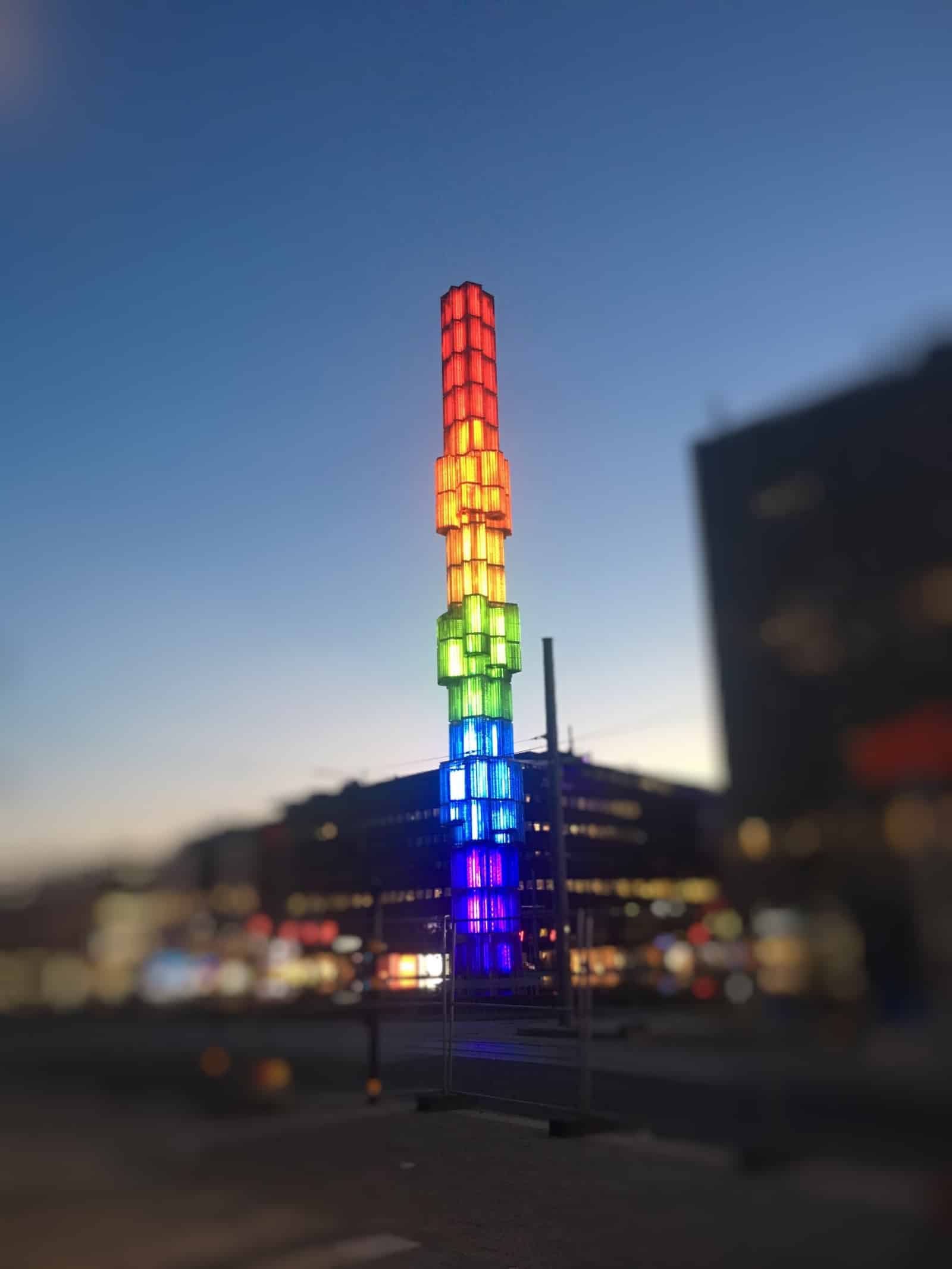 a modern statue in rainbow colors at a square at night