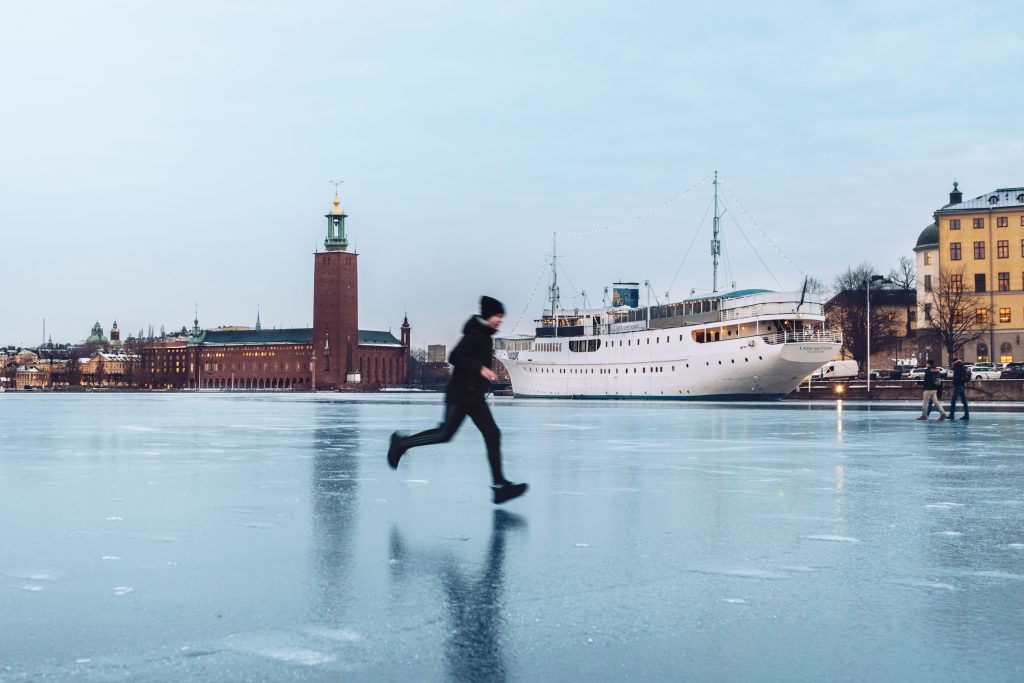 Man running on icy lake with Stockholms City Hall rising in the background at the shore