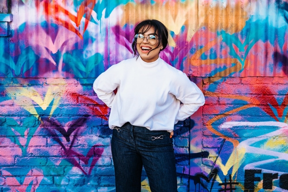 Young woman smiling and standing in front of a grafitti wall